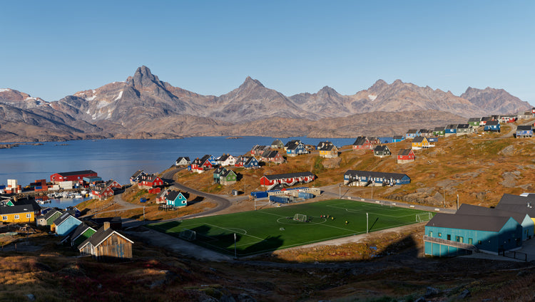 Colourful houses and a football pitch overlooking the water and mountains in Tasiilaq, Greenland.